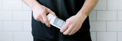 An image of a man's hands holding Schmidt's charcoal and magnesium deodorant against a tile backdrop